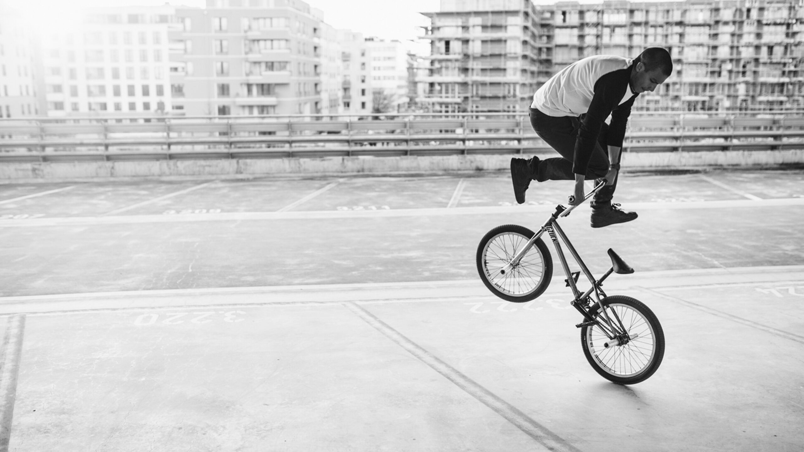 a BMX athlete is practicing his tricks in a parking lot, residential buildings can be seen in the background.