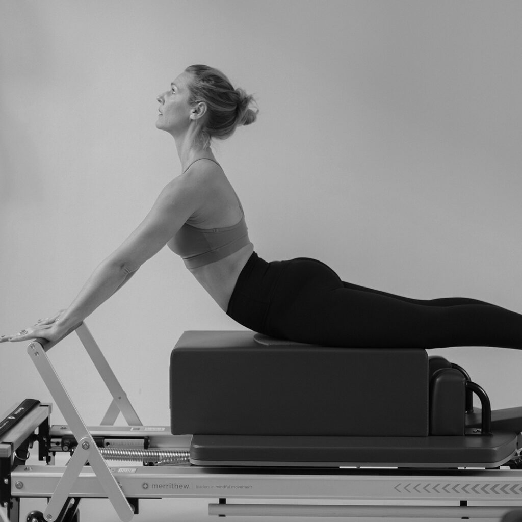 A woman trains the Pilates exercise Swan on the Pilates reformer in the Pilates studio.