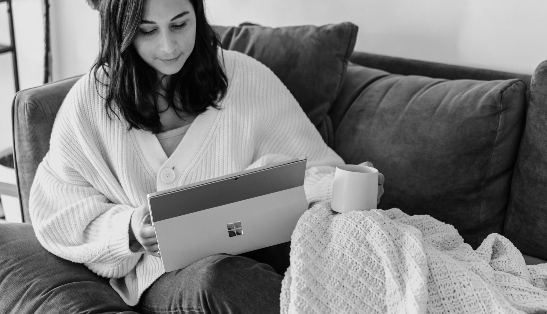 A young woman is sitting with her laptop on the sofa. The new home office of today, embodies a young woman at home.