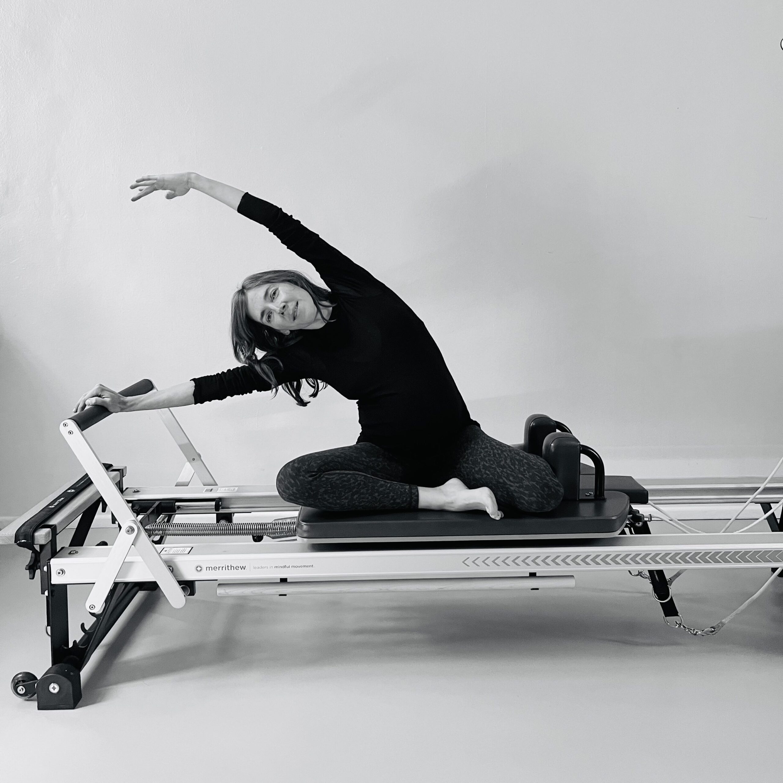 A pregnant woman stretches over her side on the Pilates reformer and enjoys the side stretch.