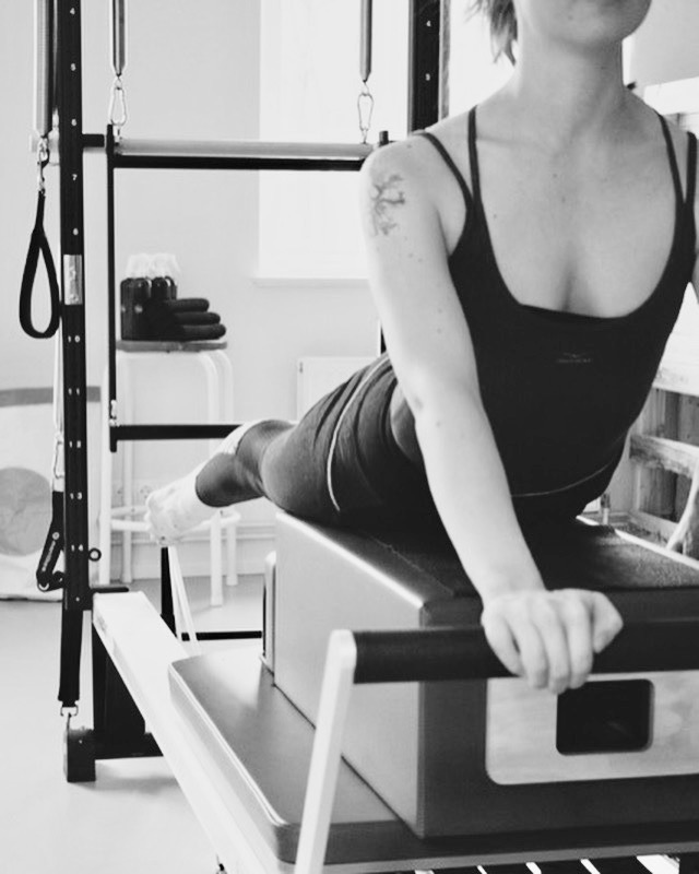 Pilates Reformer Training für ein starkes Immunsystem. Eine junge Frau stützt sihc mit ihren Armen von der Fußstange ab. Kraftvoll.