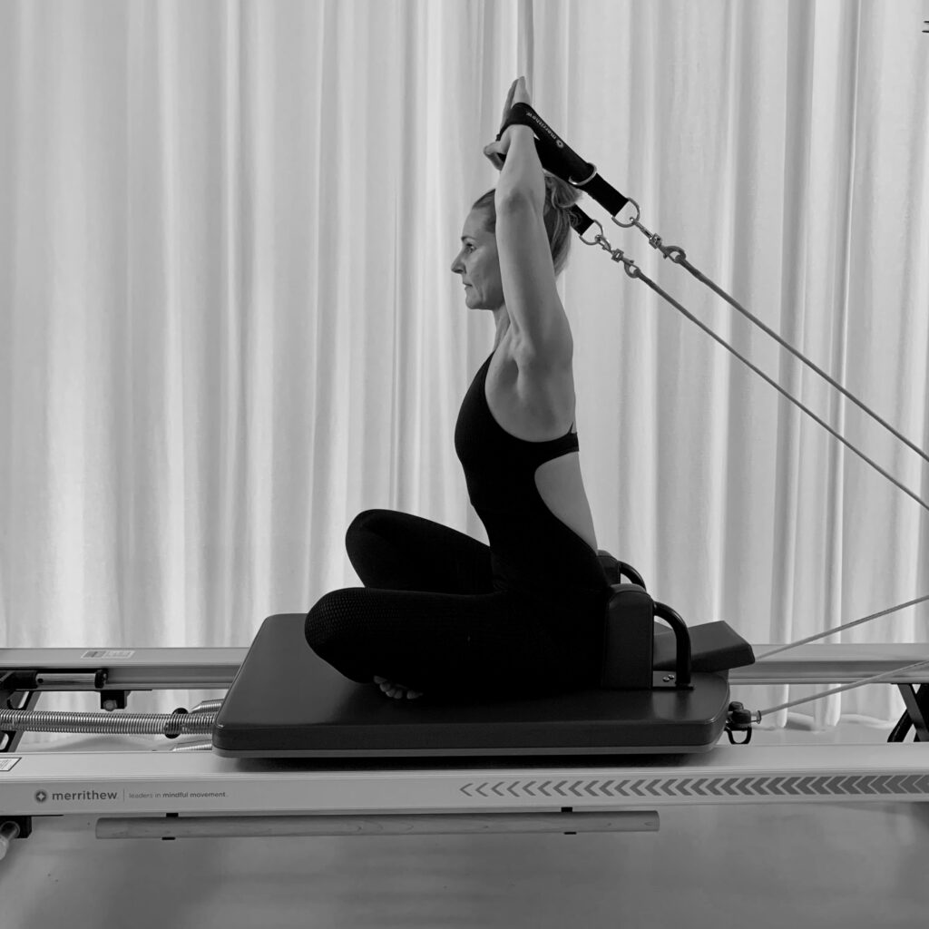 A young woman performs a Pilates exercise on the Pilates Reformer, Salute. Her hands are in the loops above her head. For an overall strengthening of the body, healthy posture. Pilates a whole body workout. 
