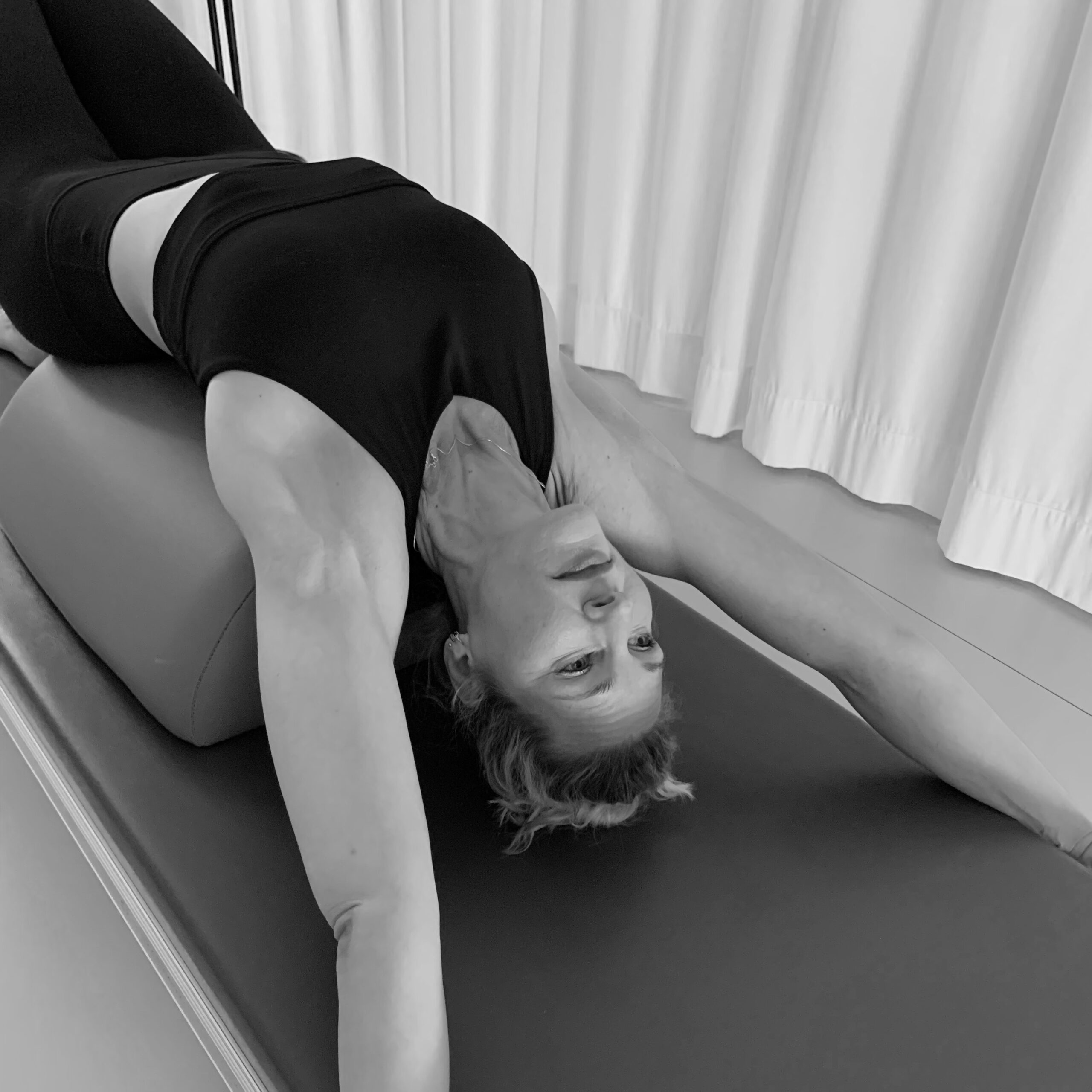 A young woman stretches over the Arc Barrel and enjoys the chest opening in the Pilates Tower Unit workout. Stretching and strengthening the body.