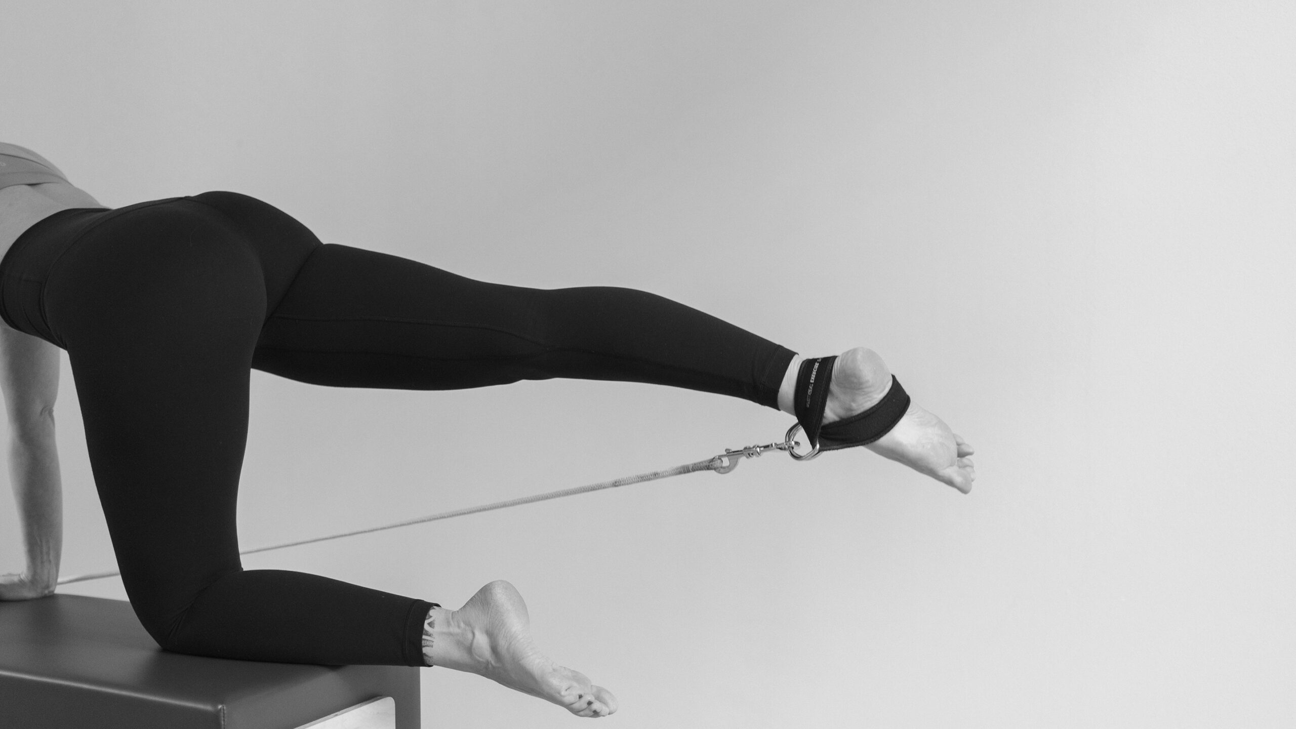 Reformer Pilates training, one foot is extended long in the footstrap, the other leg firmly anchored on the box. Straight alignment of the pelvis. Movement heals to reduce depression.