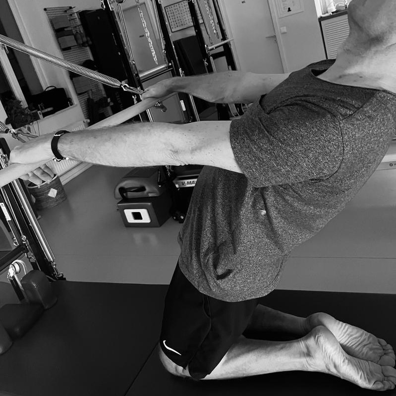 Pilates Tower Unit workout for men, leaning back with the barre to open the chest and feel the deep stretch.