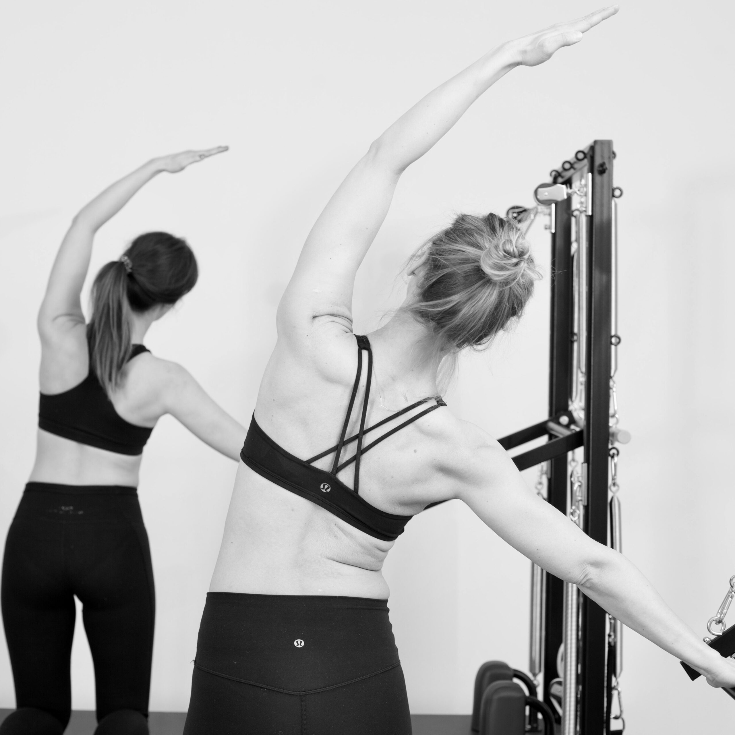 Lateral fascia stretch on the Pilates Tower Unit Wall. Two women practising Pilates fascia training.