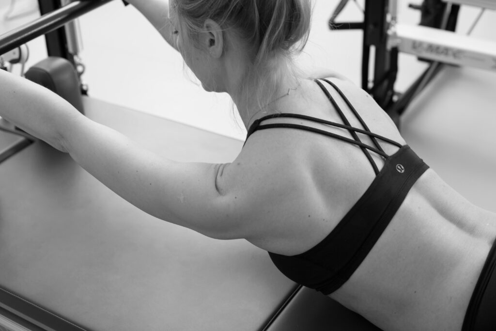 eine junge Frau führt bedacht die Pilates Haltungsübung zur kräftigung der Oberkörpermuskulatur aus. 