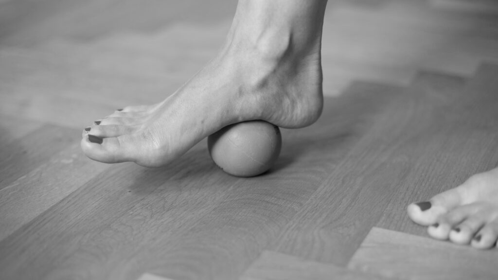 Pilates Faszientraining. Verspannungen der Füße lösen mit einem Faszienball. Der Ball liegt dabei unter der Fußsohle. 