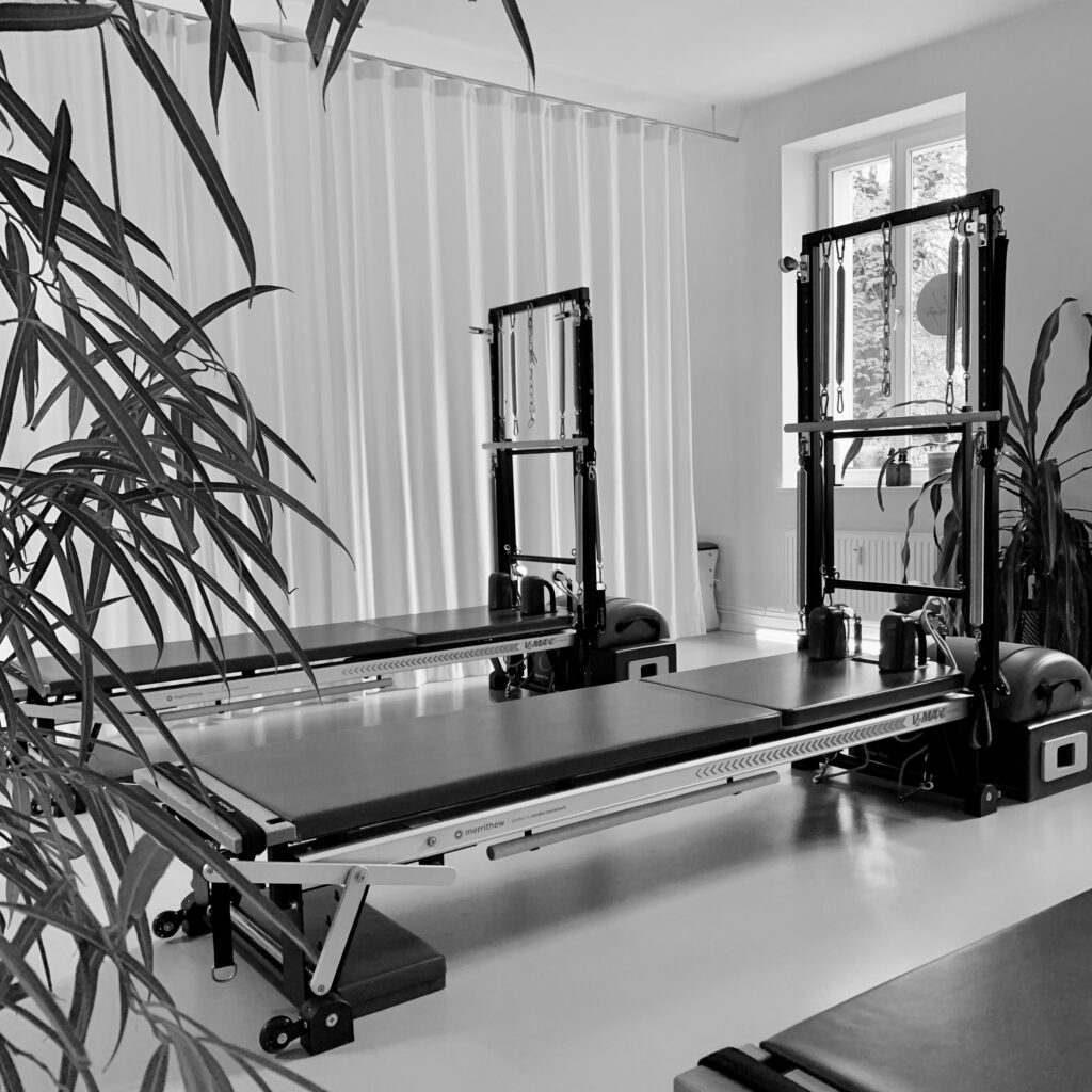 An elegant Pilates equipment studio, equipped with Pilates reformers and Pilates Tower Unit equipment. Surrounded by many plants and a green atmosphere. REALZ Pilates Studio Berlin with bright rooms.