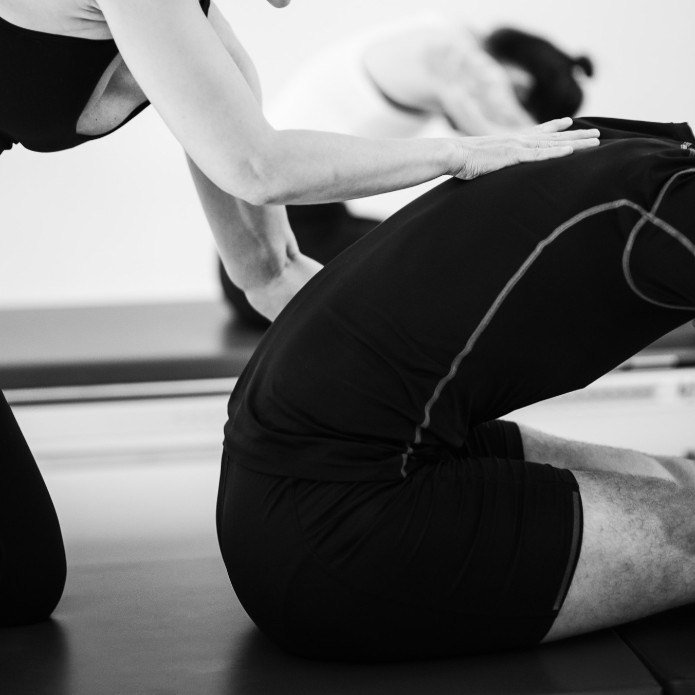 Pilates stretching exercises on the Pilates machine. A young man stretches his entire upper body forwards. A Pilates teacher supports him during the exercise. Get yourself and your body moving.