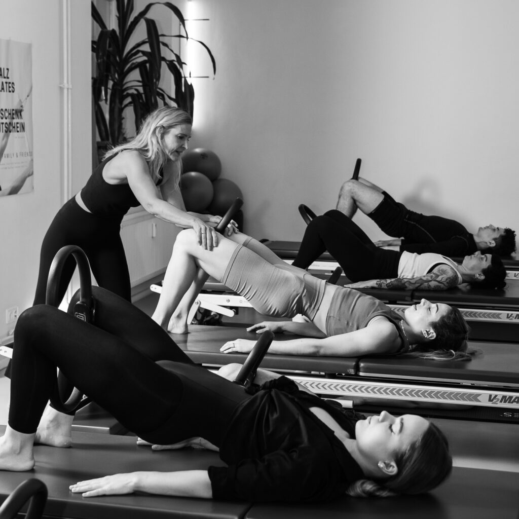 Pilates Gruppenklasse. Eine Pilates Lehrerin leitet ihre Pilates Teilnehmer durch den Unterricht. Sie liegen auf der Tower Unit, Pilates Bridging mit dem Magic Circle zwischen den Beinen um die Beckenboden und Pomuskulatur zu stärken. Die Schultern entspannen sich und lassen allen Stress los.