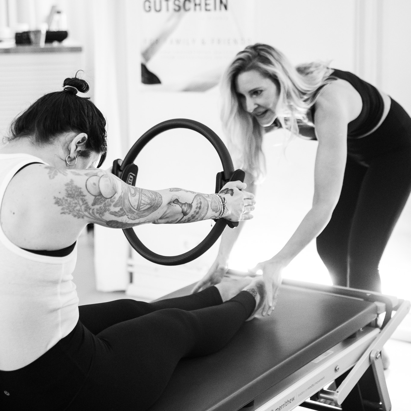 A young woman trains together with the Pilates teacher. She holds the Magic Circle in her hands and rolls on the Pilates Tower Mat to strengthen her lower back. Pilates for a slipped disc in the lower back.