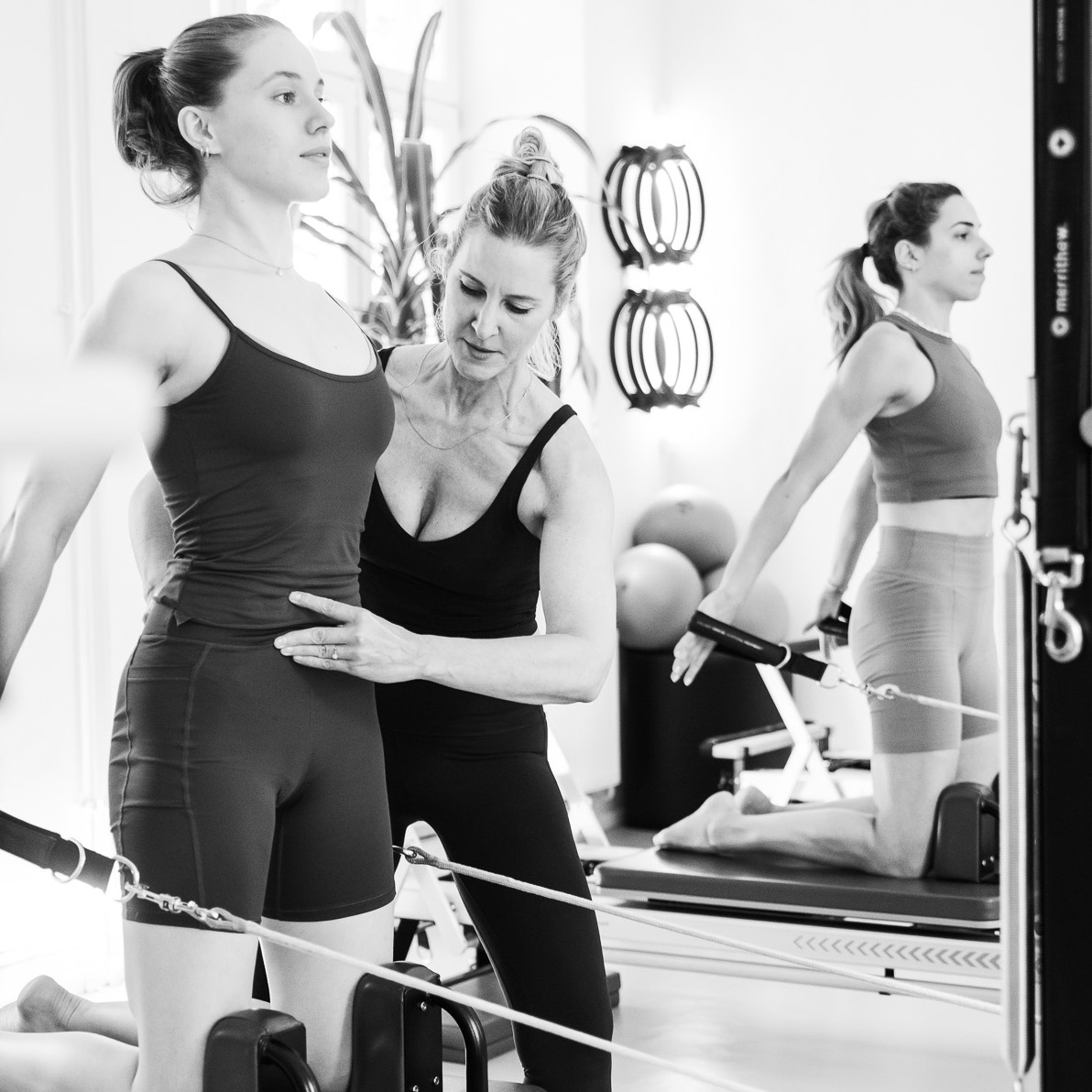 Eine junge Frau trainiert in Anleitung der Pilates Lehrerin auf dem Pilates Reformer. Das Becken ist dabei stabil, der Beckenboden aktiv und gestärkt und das Powerhouse aktiviert. Pilates Klasse in einer Gruppe. 