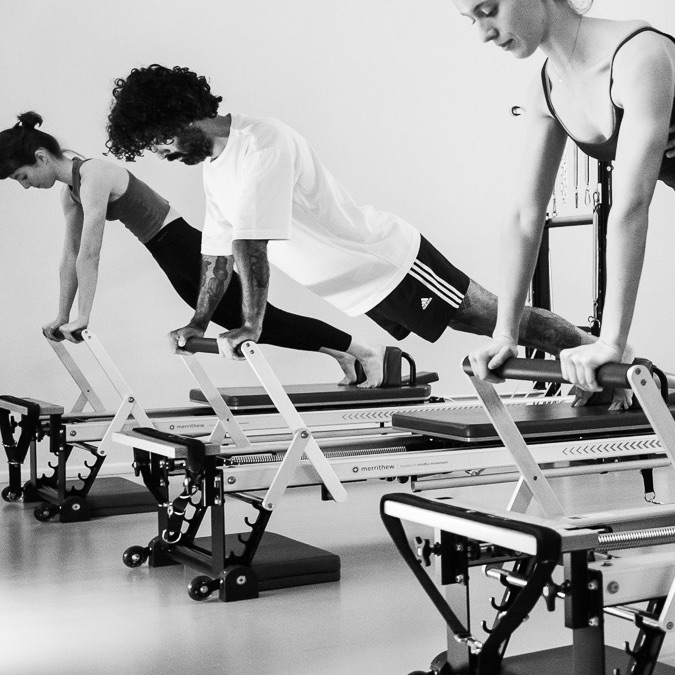 Men and women train on the Pilates reformer and are in a plank. They train their entire body and strengthen their pelvic floor muscles in the process. 