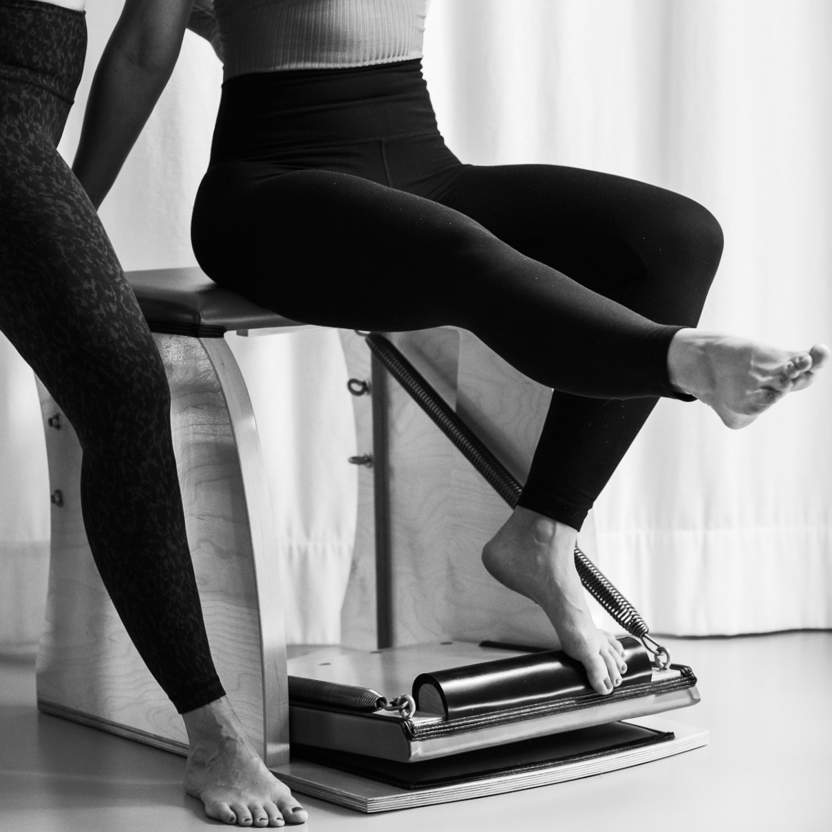 Eine junge Frau sitzt auf dem Pilates Chair und führt eine Pilates Übung für die Fuß und Beinmuskulatur aus. Mit dem Widerstand trainiert und kräftigt sie dabei ihren gesamten Fuß. Pilates Footwork Training.