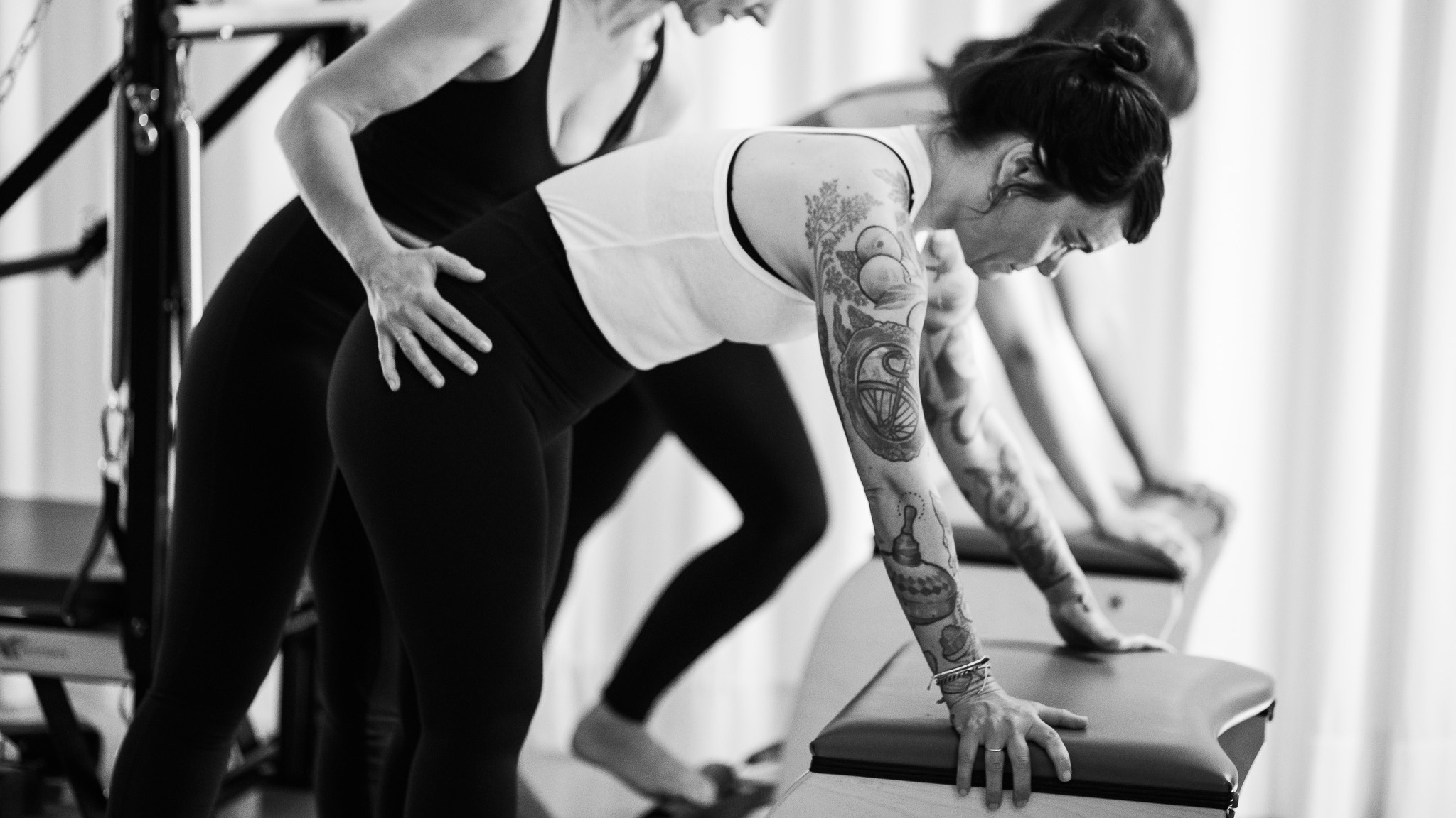 Eine Pilates Lehrerin trainiert mit zwei jungen Frauen in einer Pilates Duo Klasse am Pilates Chair Stunde. Sie befinden sich im Pilates Studio REALZ Pilates in Berlin.