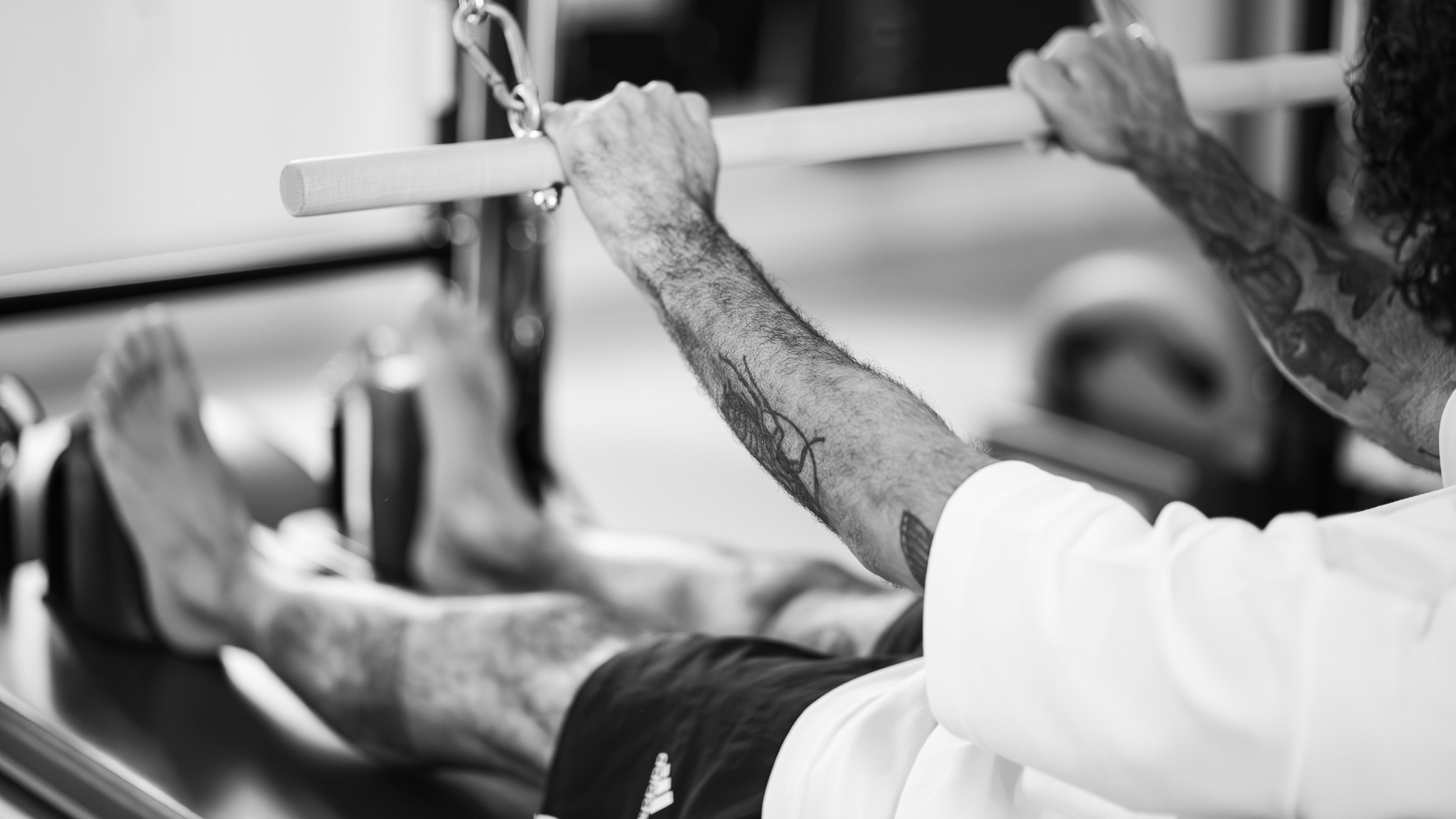 Ein sportlicher Mann trainiert an der Pilates Tower Unit Wall und genießt den Stretch. Seine Beine sind lang gestreckt und er rollt sich langsam auf der Matte ab. 