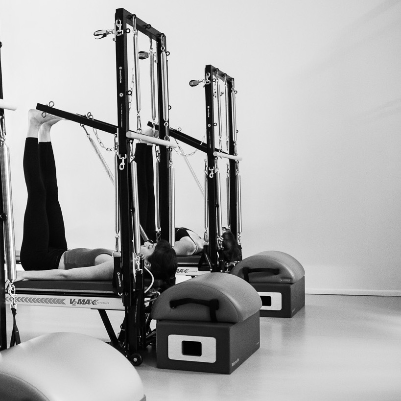Zwei junge Frauen trainieren bewusst und präzise an der Pilates Tower Unit Wall. Genießen und fühlen die Dehnung, spüren nach.