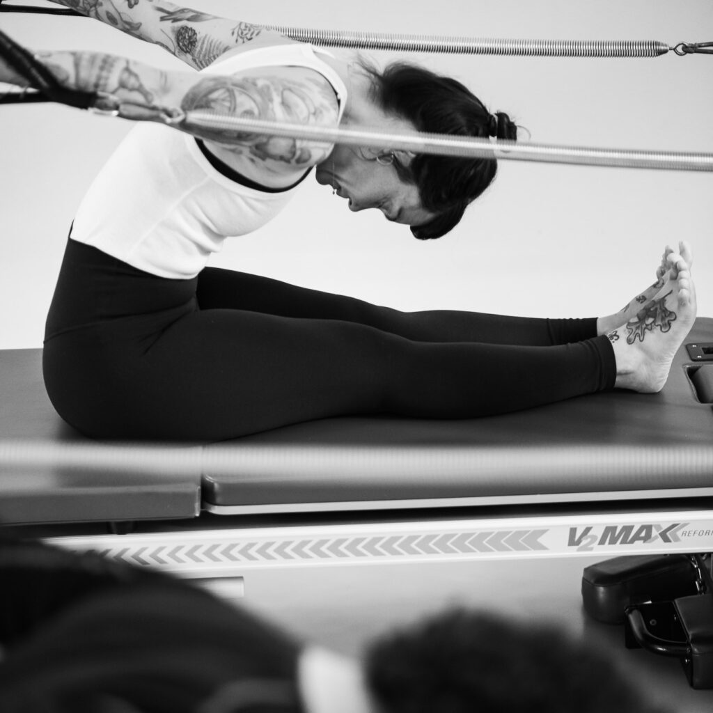 Eine junge Frau trainiert an der Pilates Tower Unit Wall, aktiv in ihrer Körperwahrnehmung mit Kraft zieht sie die Federn nach hinten. Konzentriert und stabil.
