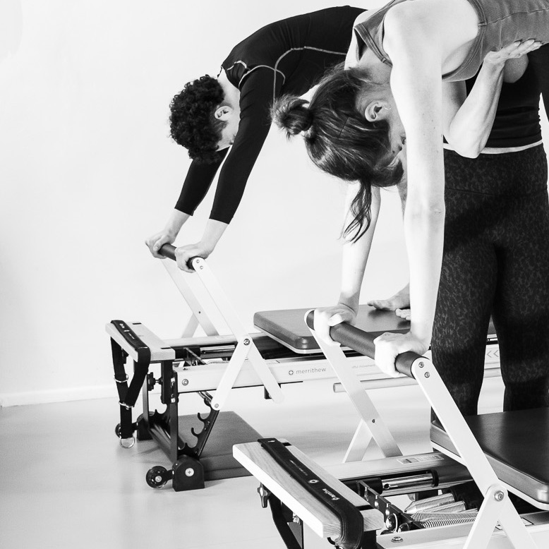Eine junge Frau und ein junger Mann trainieren gemeinsam im Pilates Reformer Training, bewusst und achtsam. Geführt und angeleitet von einer Pilates Lehrerin.