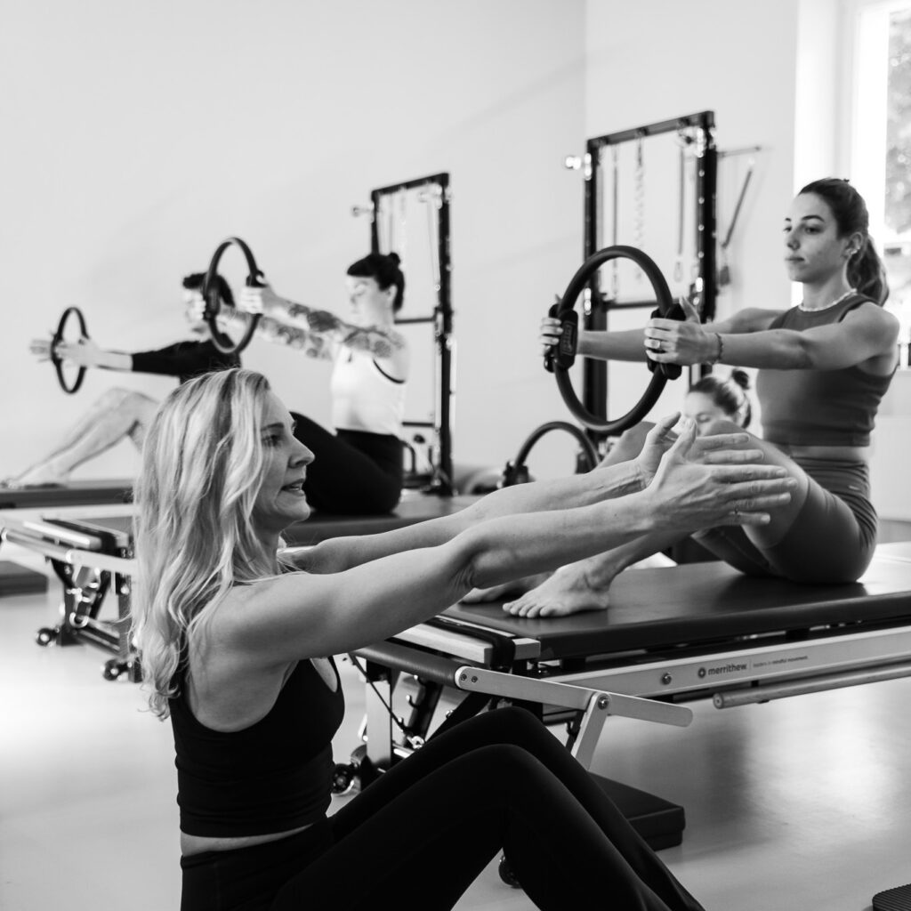 Pilates Training für Frauen 40+. Eine Pilates Lehrerin unterrichtet eine Pilates Tower Unit Klasse mit dem Magic Circle. In einer geraden aufgerichteten Körperhaltung.