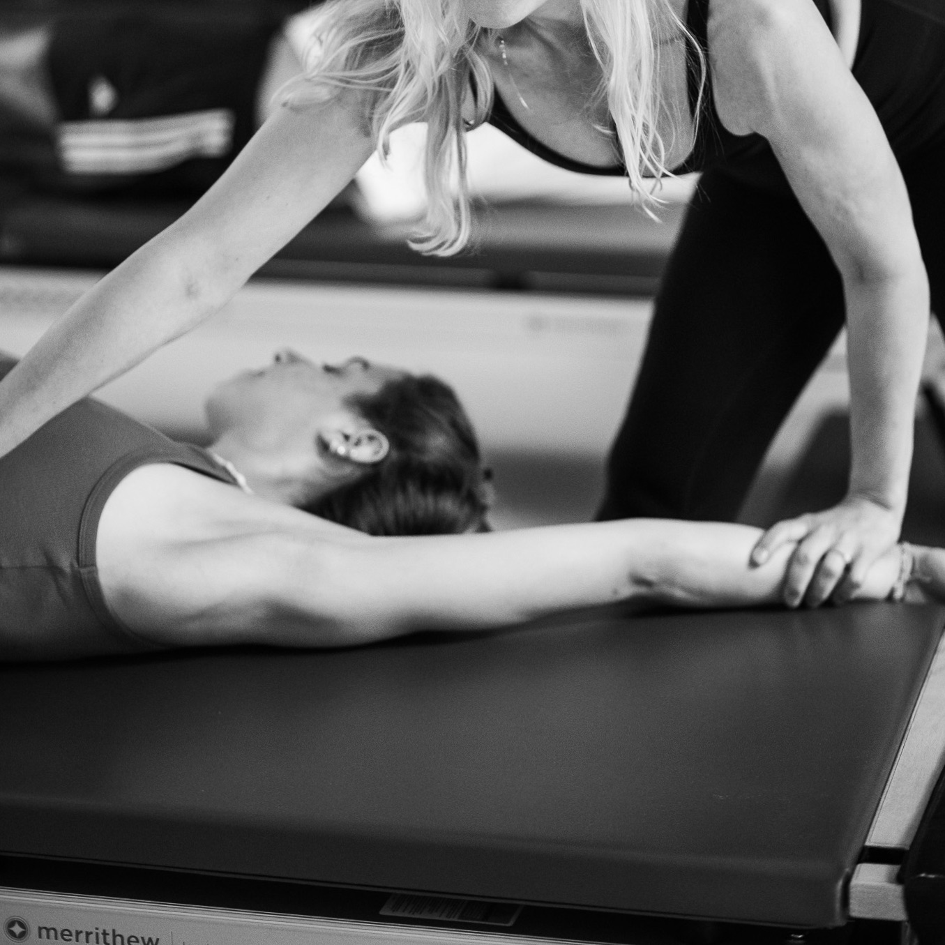 Eine Pilates Lehrerin hilft der Klienten in der Tower Unit Stunde auf um noch tiefer in die seitliche Dehnung zu spüren und Blockaden zu lösen.
