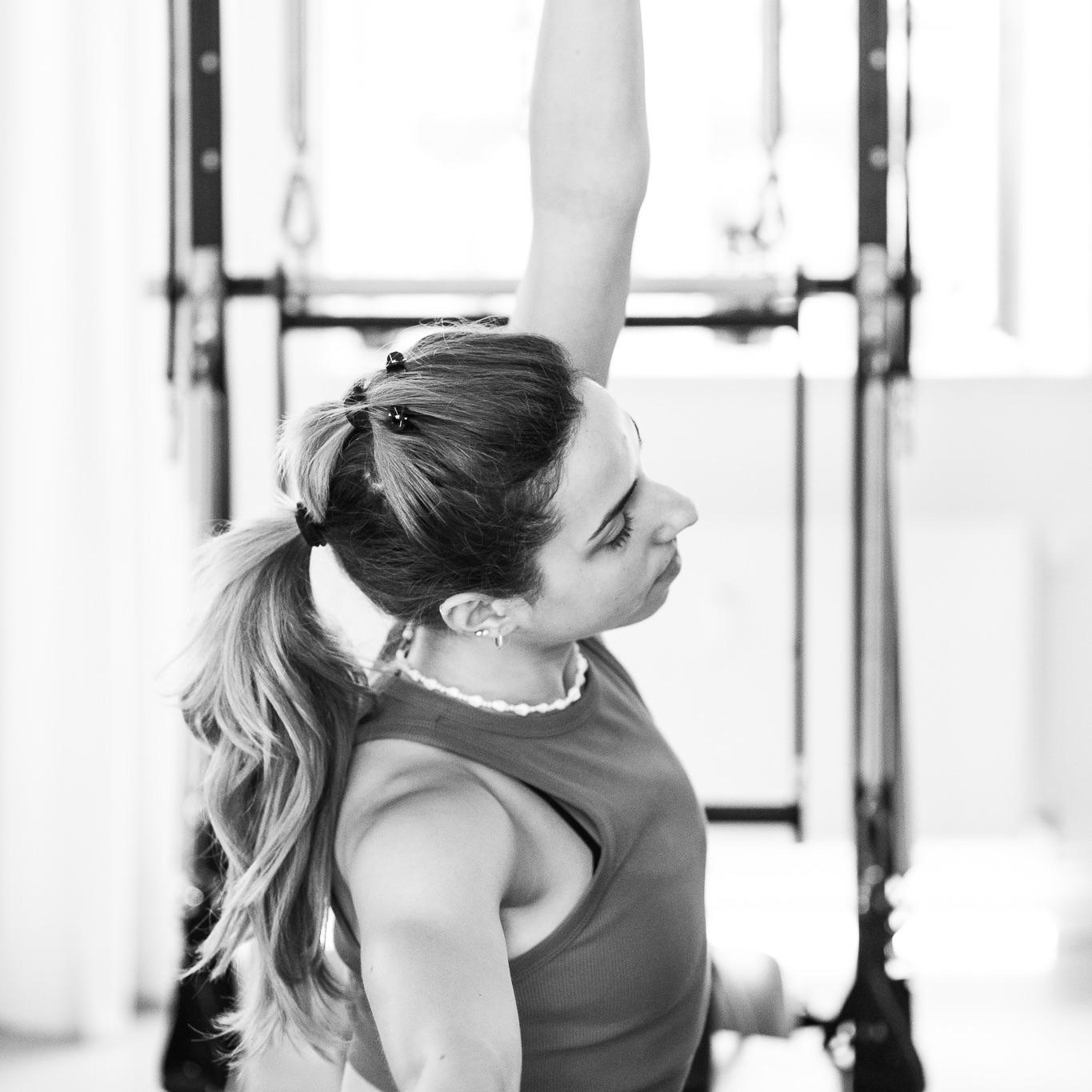 Eine junge Frau genießt die seitliche Dehnung an der Tower Unit Wall. Sie wirkt sehr entspannt und genießt das Pilates Training.