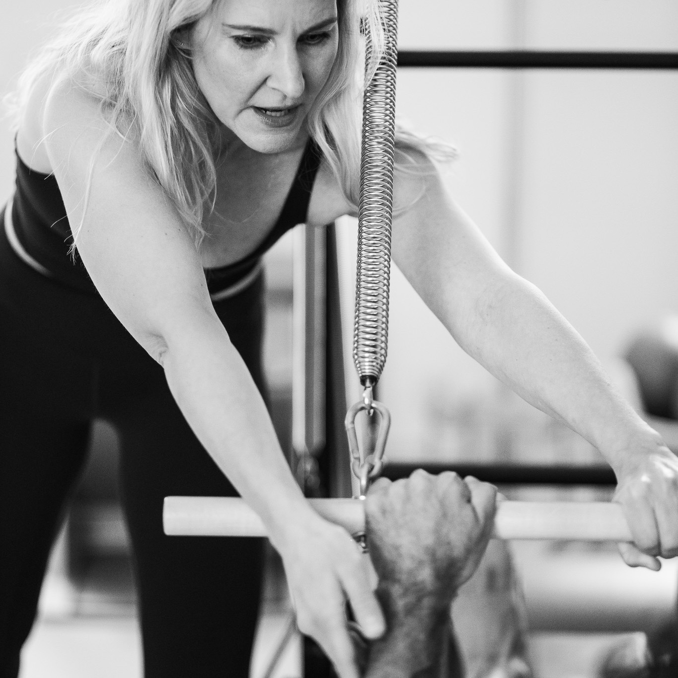 Eine Pilates Lehrerin korrigiert einen männlichen Teilnehmer am Pilates Workshop. Die Handgelenke werden begradigt mit Hilfe des Federwiderstands.